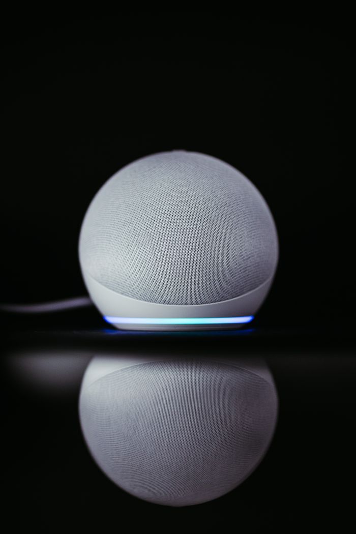 首页 A modern smart speaker Echo Dot with a sleek design and glowing base, reflected on a dark surface.